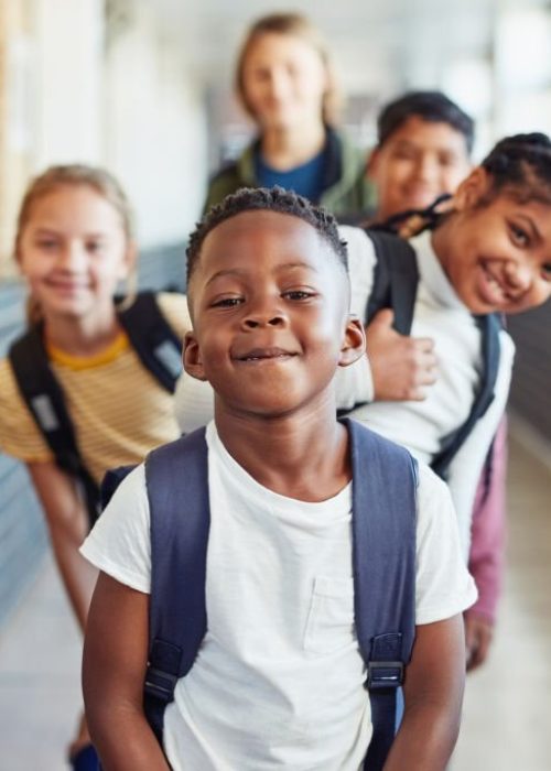 Portrait of a group of young children standing in a line in the hallway of a school