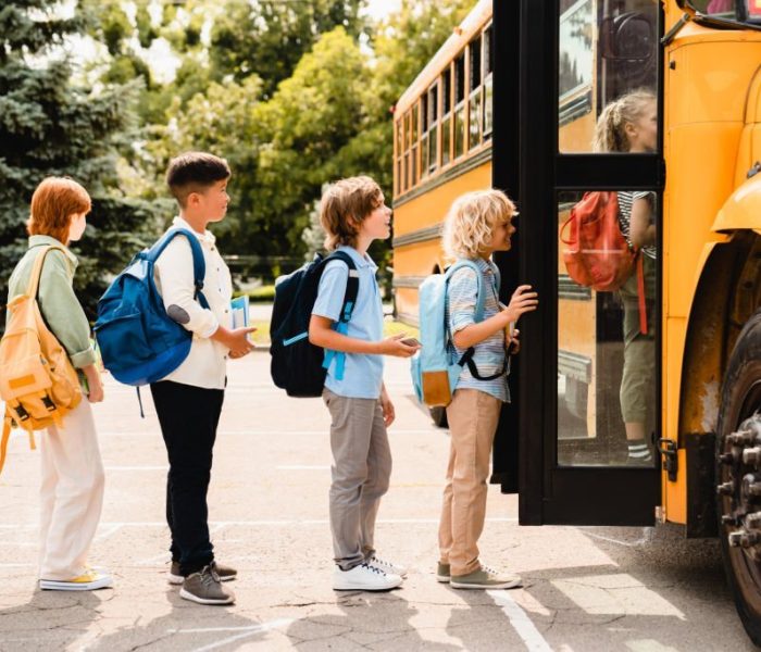 Multiethnic mixed-race pupils classmates schoolchildren students standing in line waiting for boarding school bus before starting new educational semester year after summer holidays